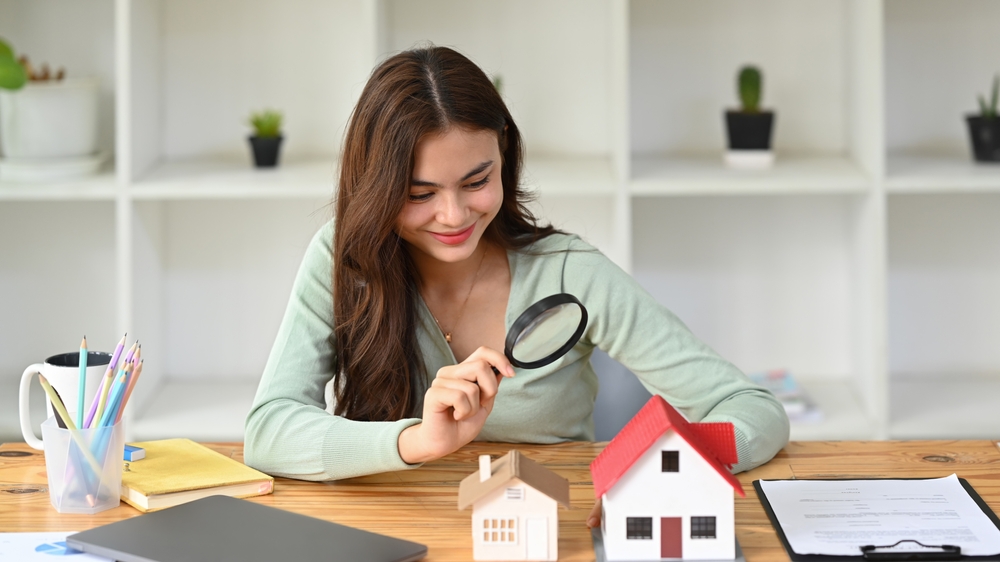 Smiling,Female,Appraiser,Looking,At,House,Model,Through,Magnifying,Glass.